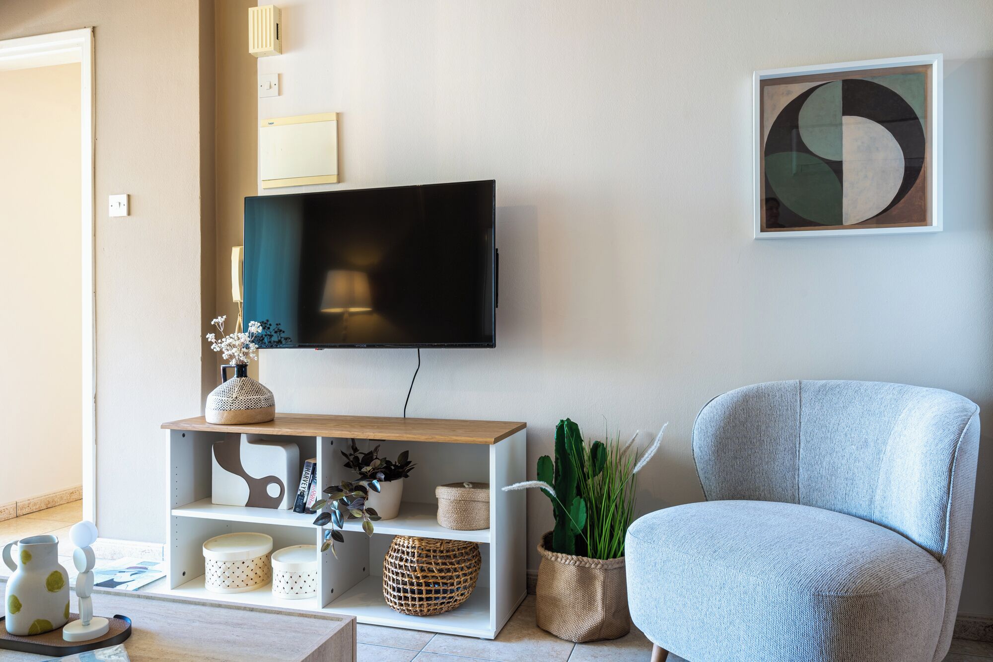 Ein Wohnzimmer mit einem an der Wand befestigten Flachbildfernseher, einem hellblauen Sessel und einem Holzkonsolentisch mit Dekorationselementen.