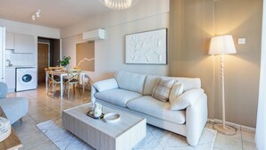 A modern living room with a light-colored sofa, a coffee table, and a dining area with a table and chairs. - Calina - 3-BR Apt & Pool in Mackenzie (Larnaca)