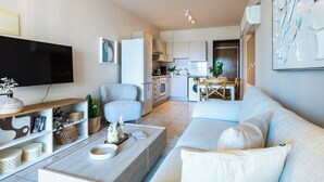 A modern living room with a sofa, coffee table, and a flat-screen TV. - Calina - 3-BR Apt & Pool in Mackenzie (Larnaca)