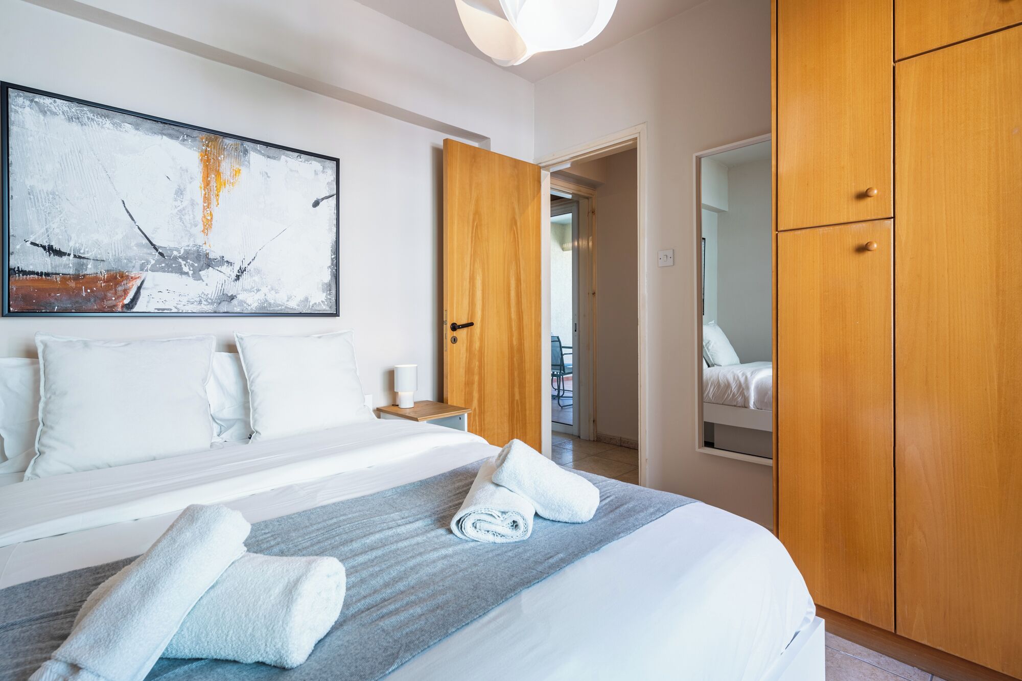 Une chambre d’hôtel avec un grand lit, un tableau accroché au mur, une armoire en bois et une salle de bain visible à travers une porte ouverte.