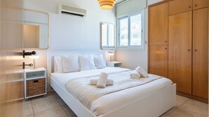 A bedroom with a bed, bedside tables, a wardrobe, a hanging light fixture, and a window. - Calina - 3-BR Apt & Pool in Mackenzie (Larnaca)