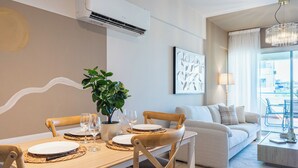 A dining area with a table set for four, a potted plant, and a modern air conditioning unit above the table. - Calina - 3-BR Apt & Pool in Mackenzie (Larnaca)