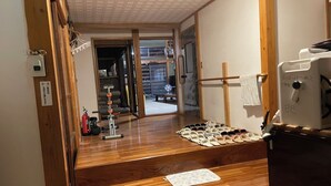 A room with a wooden floor, a small table with shoes, a fire extinguisher, and a door leading to another room. - Echigo-Tsumari Art Triennale near the ski resort. (Tokamachi)