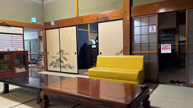 A traditional Japanese room with tatami flooring, a wooden table, a yellow sofa, sliding doors, and a clock on the wall. - Echigo-Tsumari Art Triennale near the ski resort. (Tokamachi)