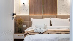 A neatly made bed with rolled towels and a bedside table with a vase of dried plants. - Golden Hour Residence - Elegant Cityview Apartment in Historic Bucharest (București)