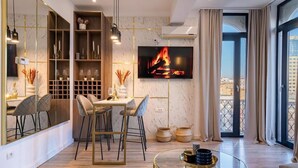 A modern living room with a TV, dining area, and large windows. - Golden Hour Residence - Elegant Cityview Apartment in Historic Bucharest (București)
