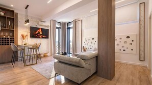 A modern living room with a sofa, a dining area with a table and chairs, a TV mounted on the wall, and a large window with curtains. - Golden Hour Residence - Elegant Cityview Apartment in Historic Bucharest (București)