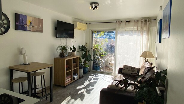 En stue med sofa, sofabord, fjernsyn og bogreol. Der er en skydedør, der fører ud til en terrasse med planter.