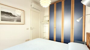 Ein Schlafzimmer mit Bett, Schrank, einer Pendelleuchte und einem gerahmten Bild an der Wand.
