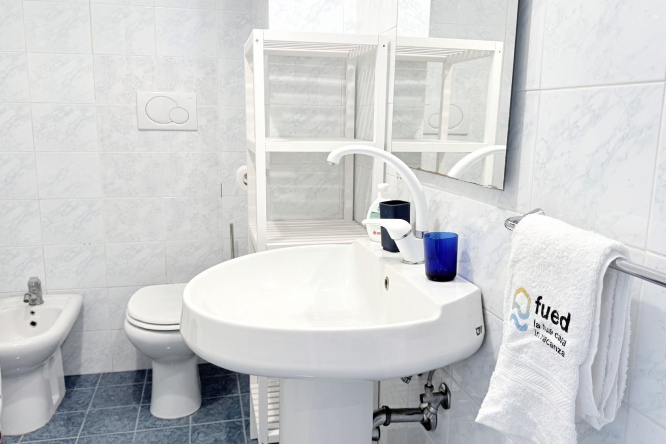 A bathroom with a white sink, toilet, and bidet. There is a towel rack with a towel hanging on it.