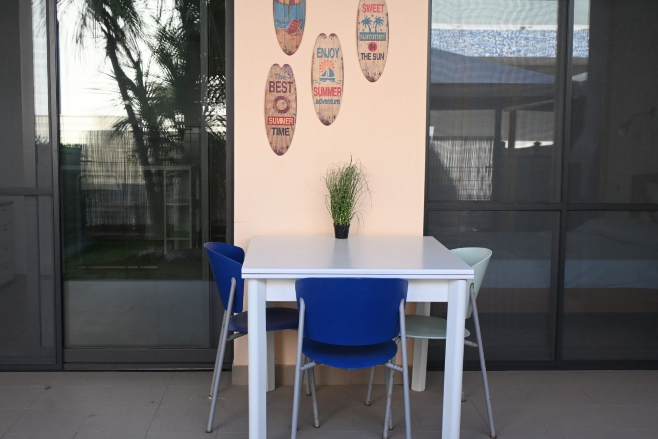 A white table with blue chairs, a potted plant, and wooden wall decorations with summer-themed text.