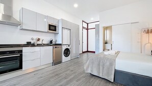 Una cocina moderna con electrodomésticos integrados, un comedor y un dormitorio con cama y mesita de noche.