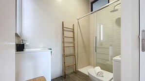 Un baño con inodoro, ducha, toalla, escalera y un lavamanos pequeño.