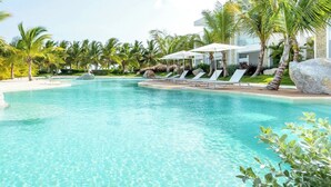 Ein Swimmingpool mit Liegestühlen und Sonnenschirmen, umgeben von Palmen und einem modernen Gebäude.