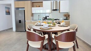 Eine moderne Küche mit weißen Schränken, einem eingebauten Backofen und einem Essbereich mit rundem Tisch und vier Stühlen.