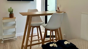 Ett modernt vardagsrum med ett matbord i trä, vita stolar, en väggmonterad TV och en krukväxt.