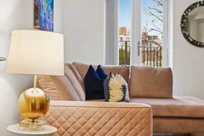 A living room with a beige sofa, a gold lamp, and a view of the outside. - Victoria Grove Light & Bright Flat (London)