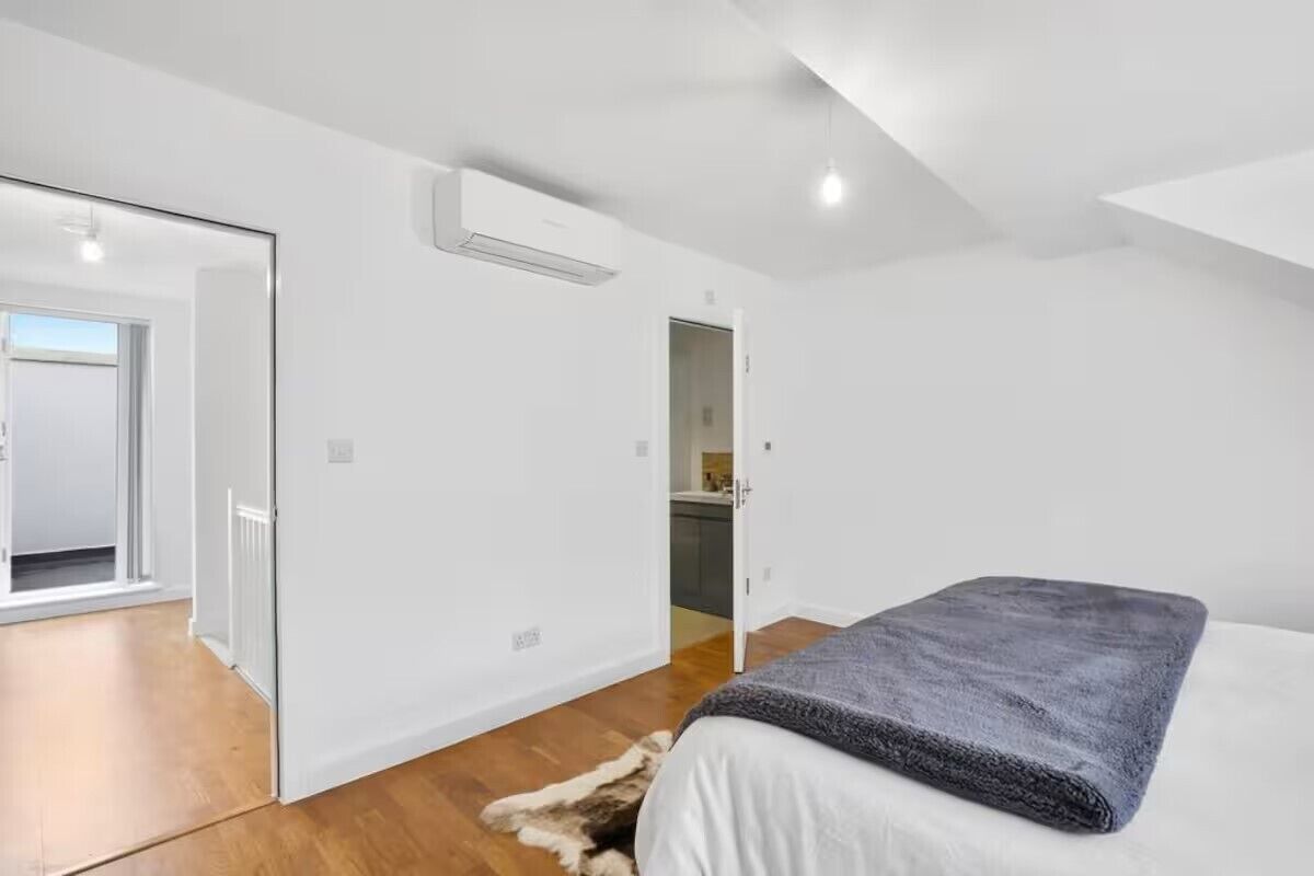 Un dormitorio moderno con una cama grande, una pared blanca y piso de madera.