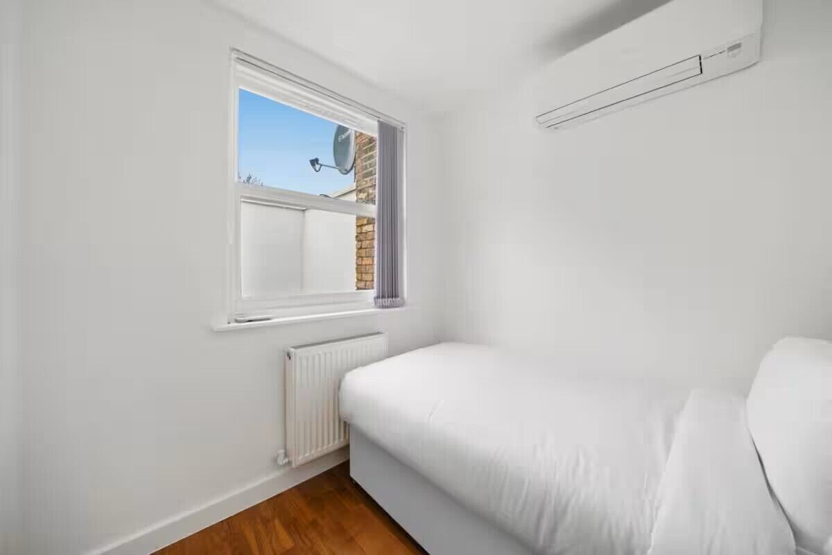 A bedroom with a single bed, a window, a radiator, and a brick wall.