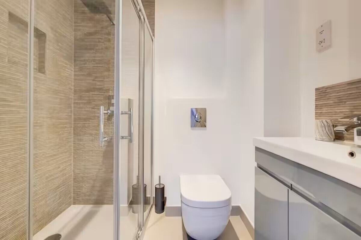 A modern bathroom with a glass shower enclosure, a white toilet, and a minimalist vanity with a mirror.