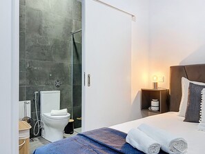 Ein modernes Hotelzimmer mit Dusche, Toilette und einem Bett mit Kopfteil.