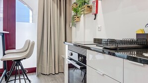 Eine moderne Küche mit weißen Schränken, einer schwarzen Arbeitsplatte und einem eingebauten Backofen. Zwei Barhocker und ein Fenster mit Vorhängen sind ebenfalls vorhanden.