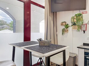Ein modernes Zimmer mit Esstisch, Stühlen, Fernseher und Topfpflanzen.