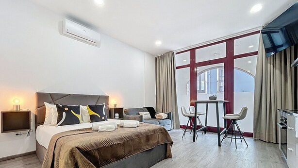 Ein modernes Hotelzimmer mit einem großen Bett, Nachttischen, einem Schreibtisch mit Stühlen und einem großen Fenster mit Vorhängen.