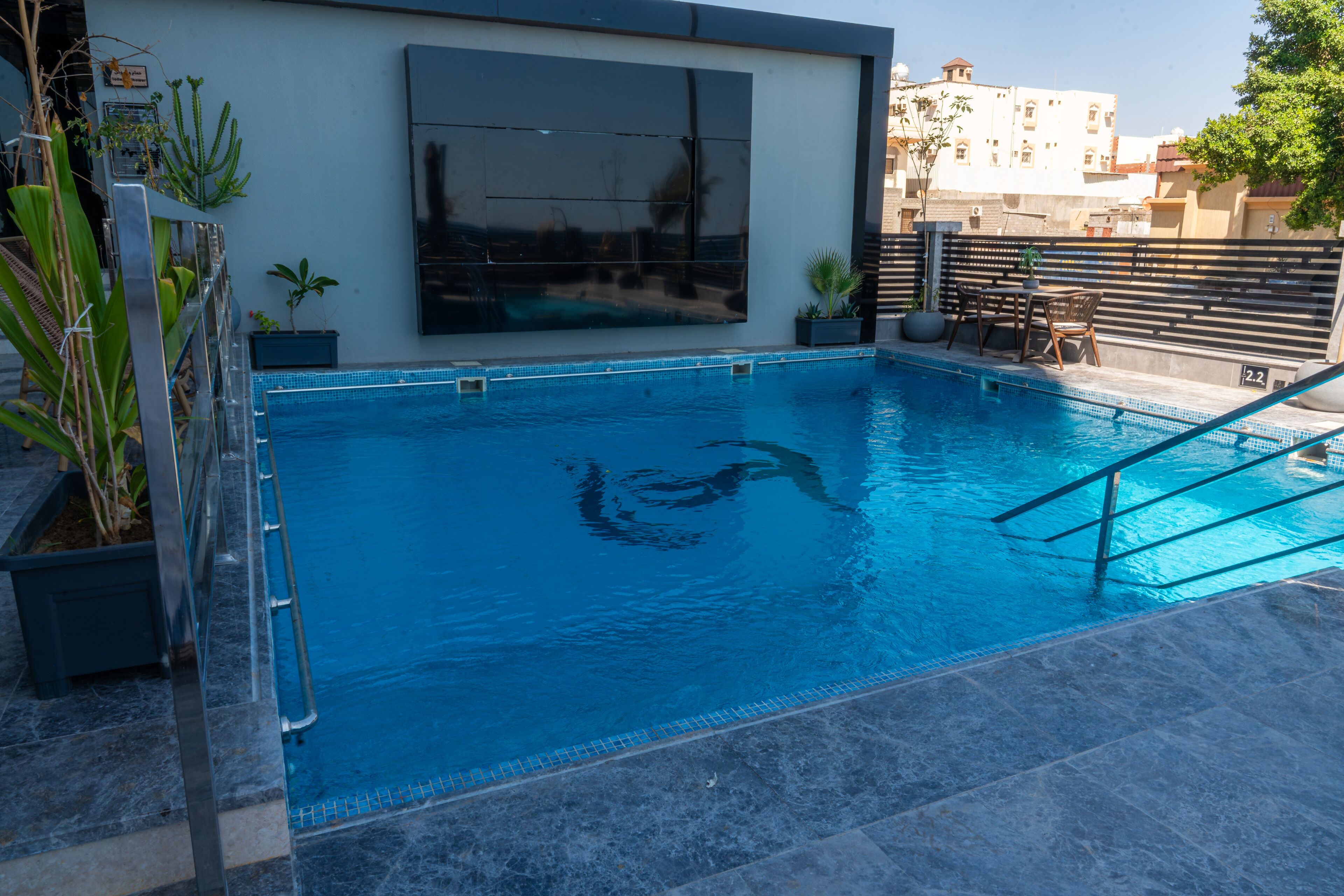 A swimming pool with a tiled edge, a metal ladder, and a seating area with a table and chairs.