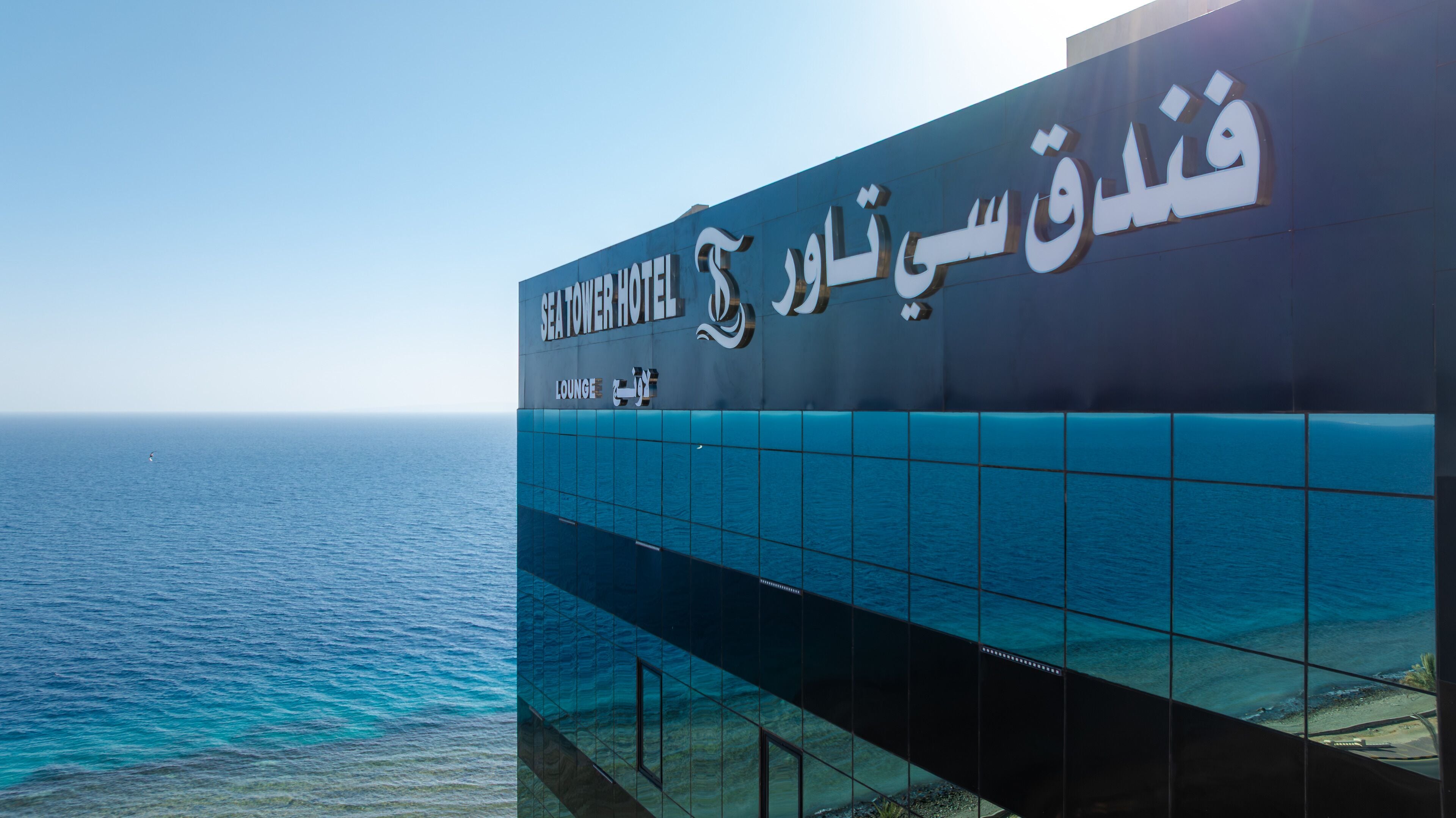 A hotel sign with Arabic text and a view of the sea.