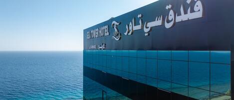 A hotel sign with Arabic text and a view of the sea.