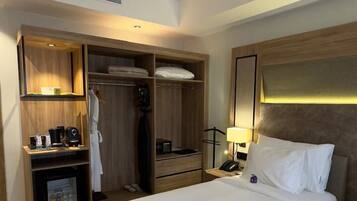 A hotel room with a large bed, a wardrobe, a desk with a lamp, and a minibar.
