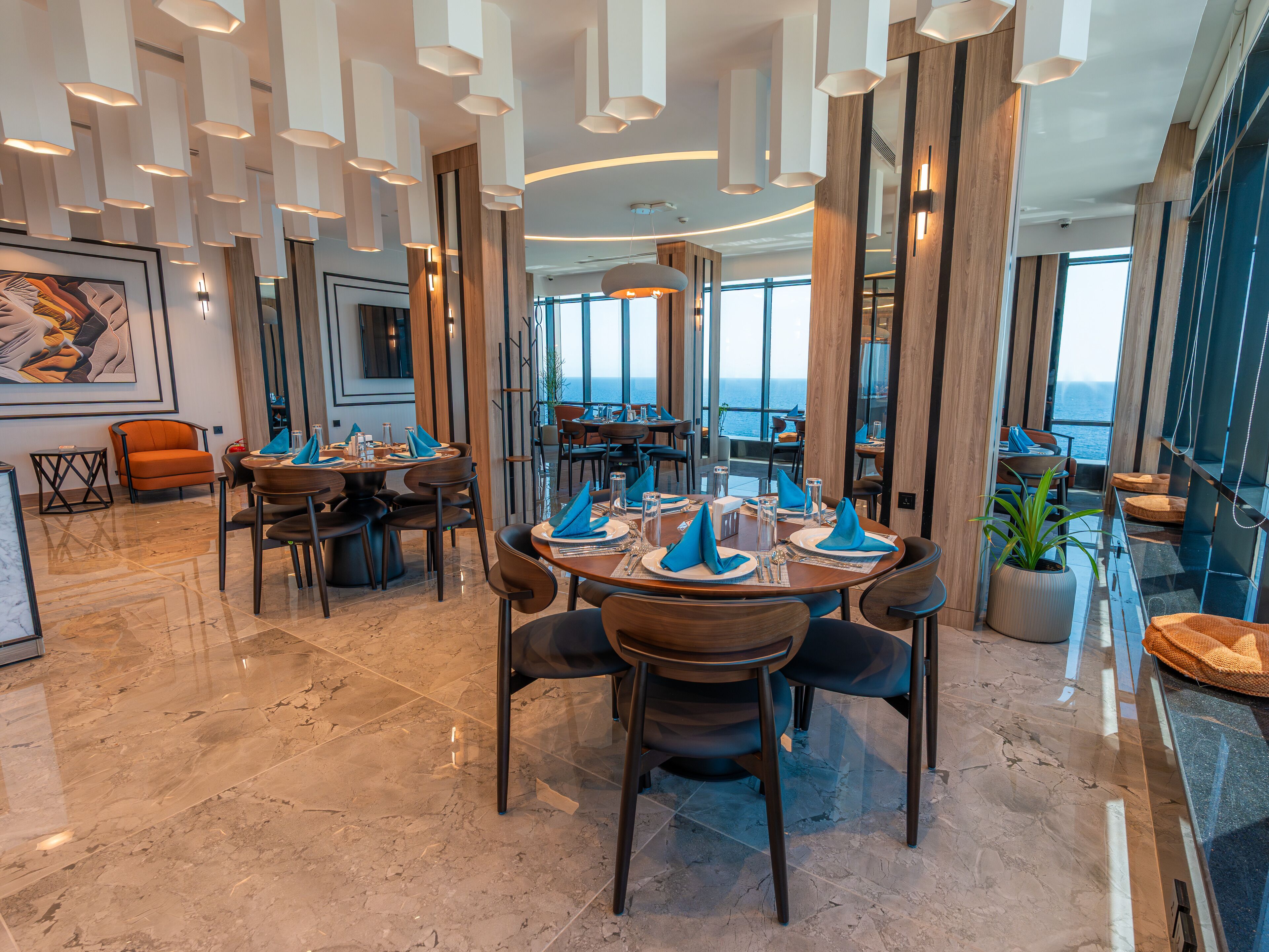 A modern dining area with round tables, chairs, and a view of the ocean.