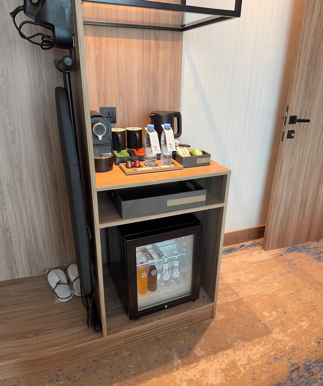 A minibar with a refrigerator, a coffee maker, and various bottles.