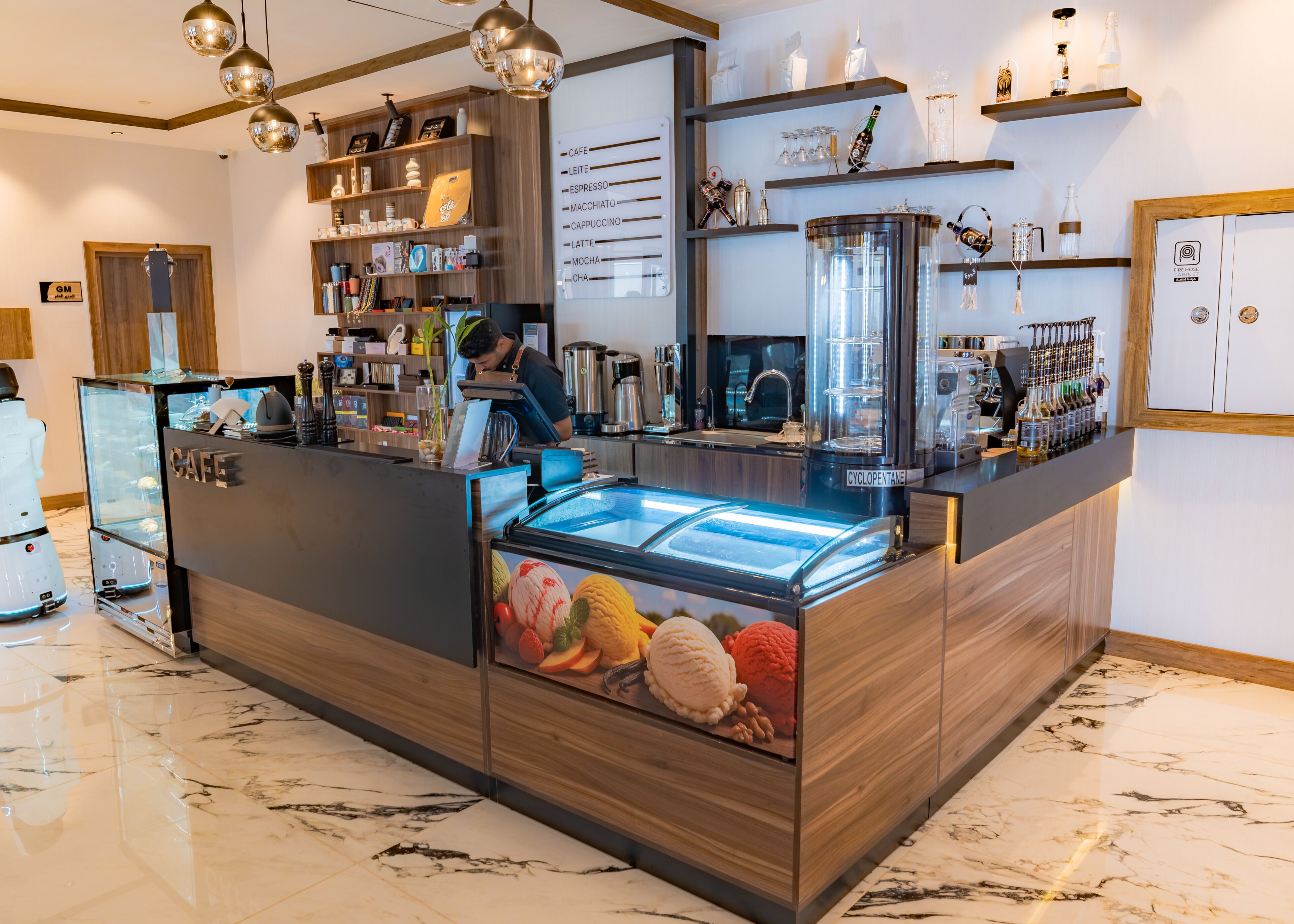 A cafe with a marble floor, a refrigerated display case with ice cream, and a bar area with various coffee machines and bottles.