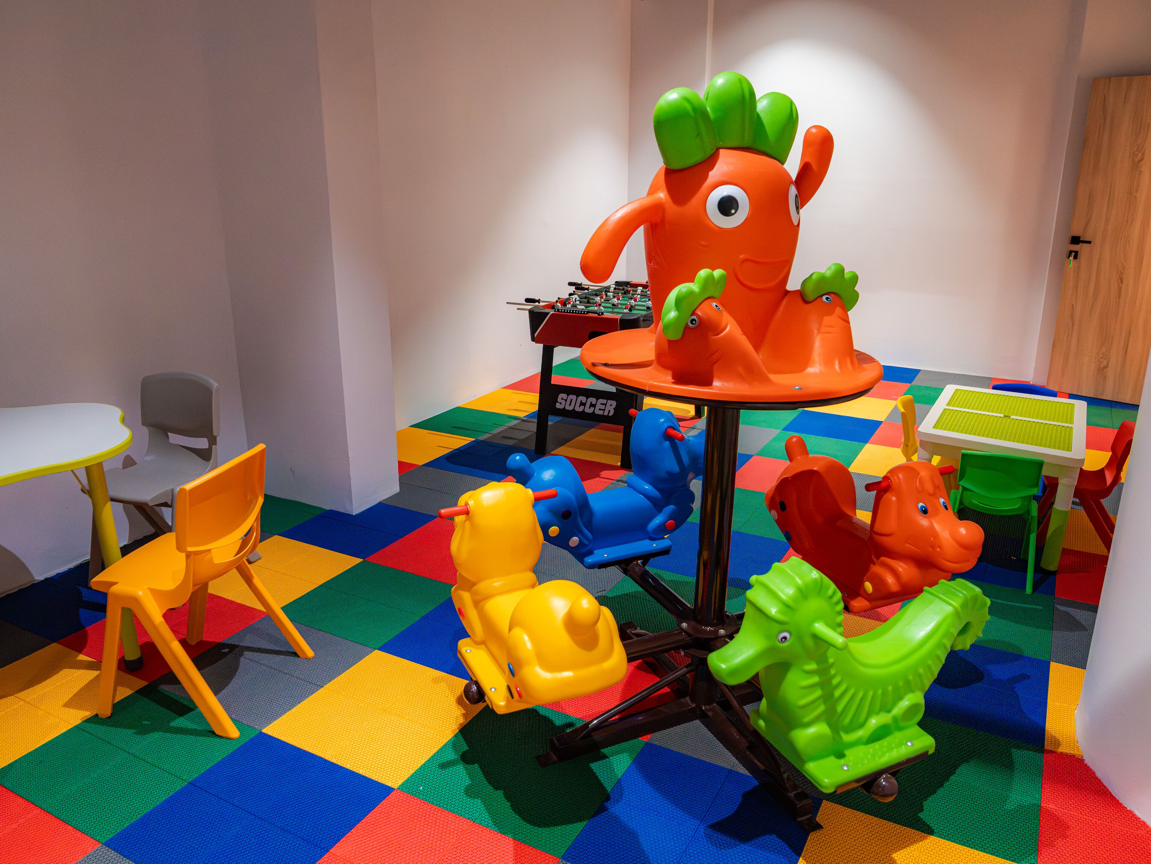 A play area with colorful play mats, a table, chairs, and various children's toys.