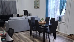 A modern living room with a grey sofa, a dining table with chairs, and a wooden herringbone floor. - Relax & Recharge: Your Dream Stay in Port Carbon! (Port Carbon)