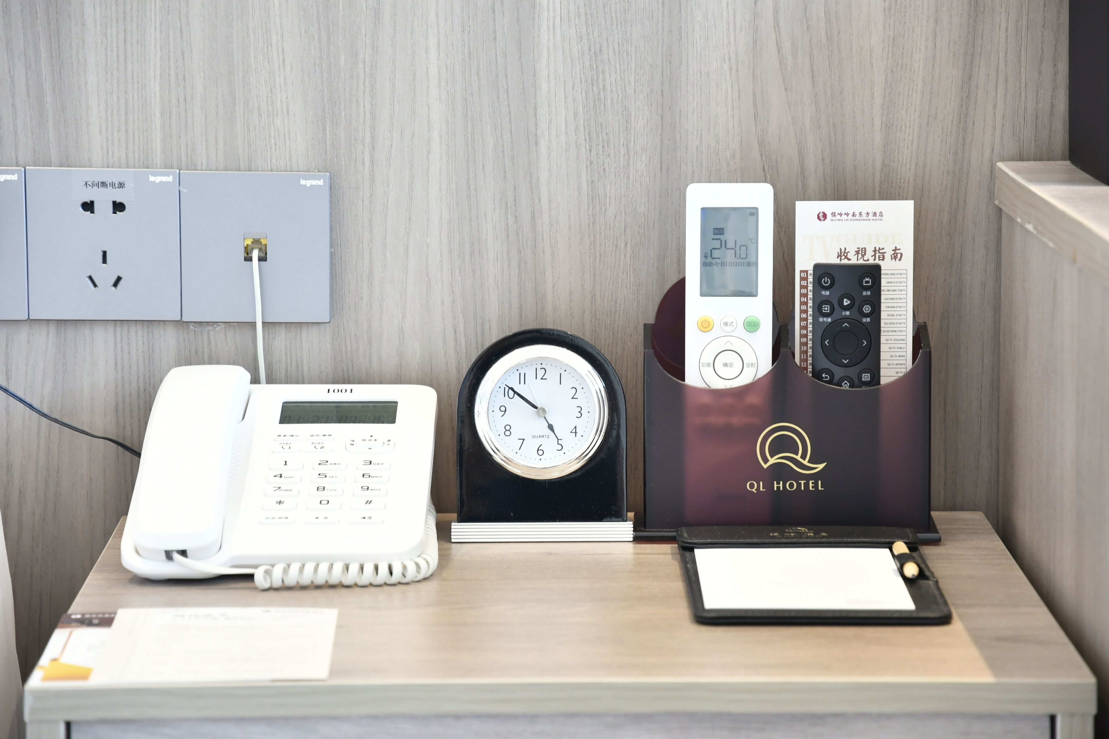 A hotel reception desk with a telephone, a clock, and a remote control.