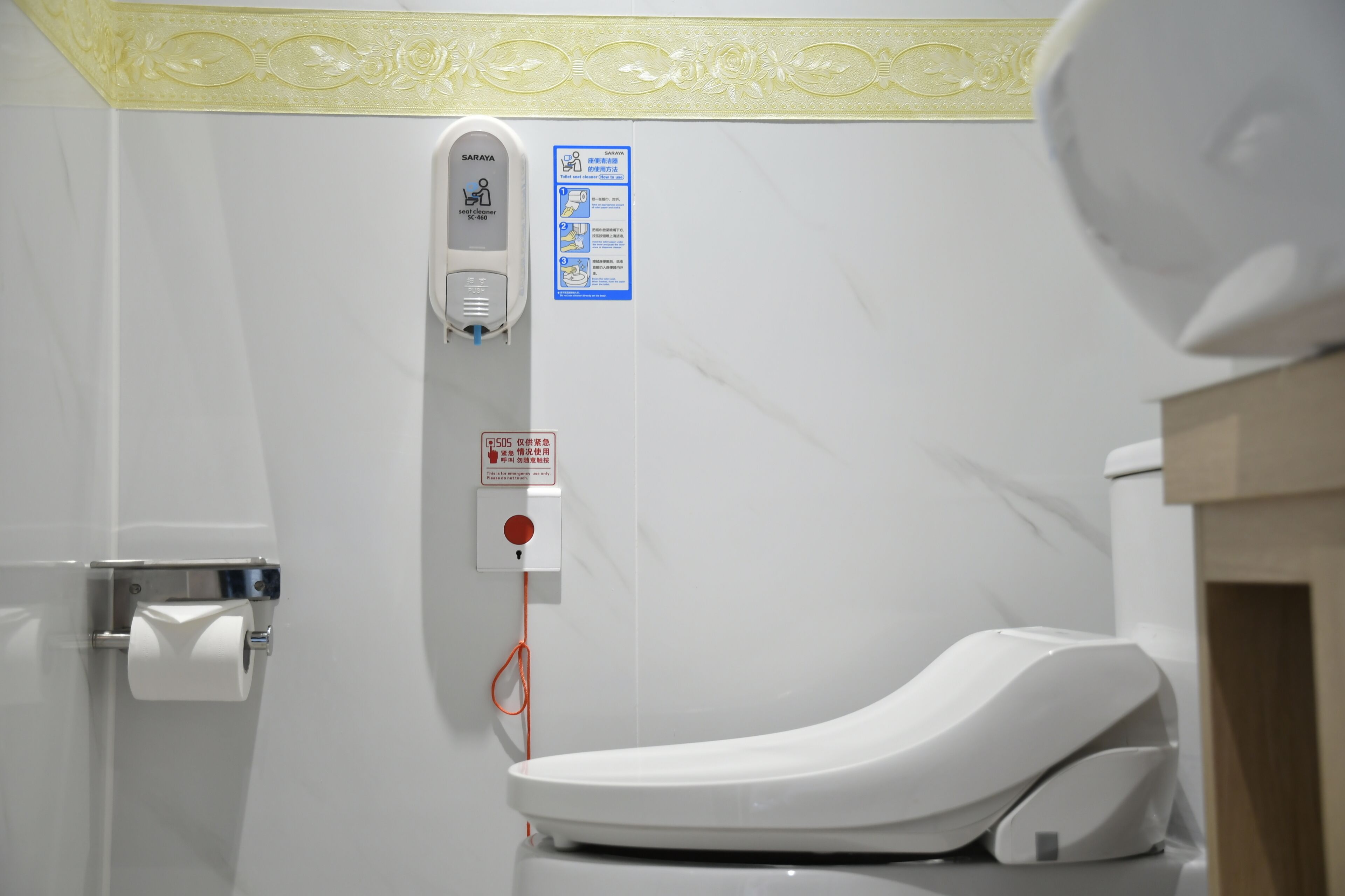 A modern bathroom with a toilet, a hand sanitizer dispenser, and a toilet paper holder.