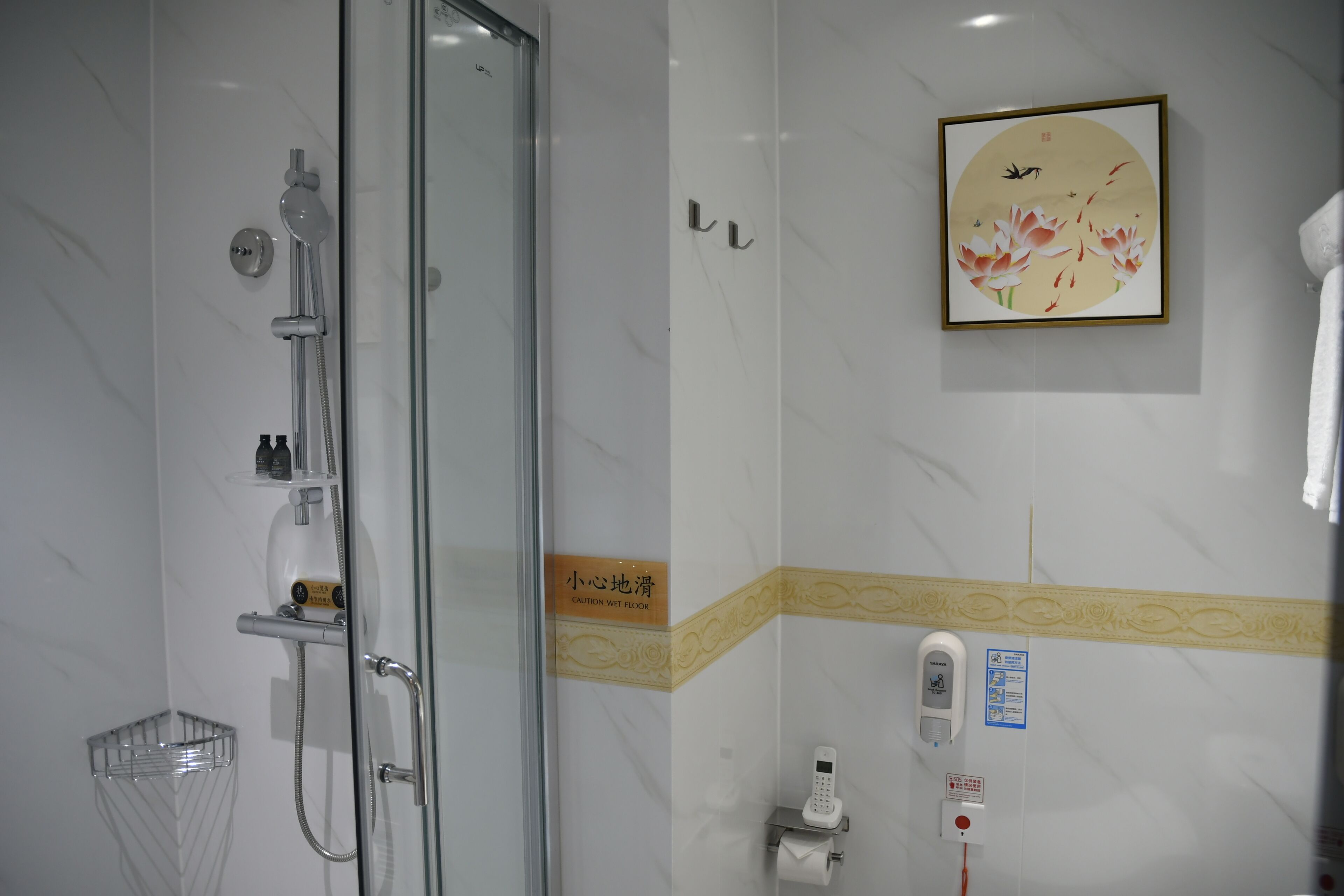 A bathroom with a glass-enclosed shower, a toilet paper holder, a hand dryer, and a framed artwork on the wall.