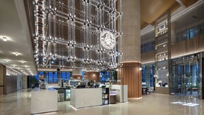 A spacious lobby with a central reception desk, modern lighting fixtures, and a large digital display. - Wanda Moments Zibo (Zibo)