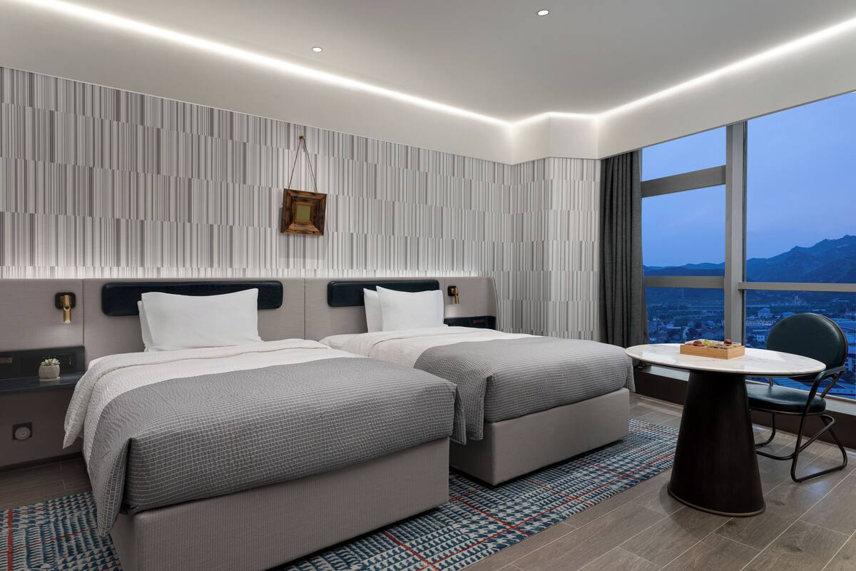 Ett modernt hotellrum med två sängar, ett matbord och utsikt över staden.