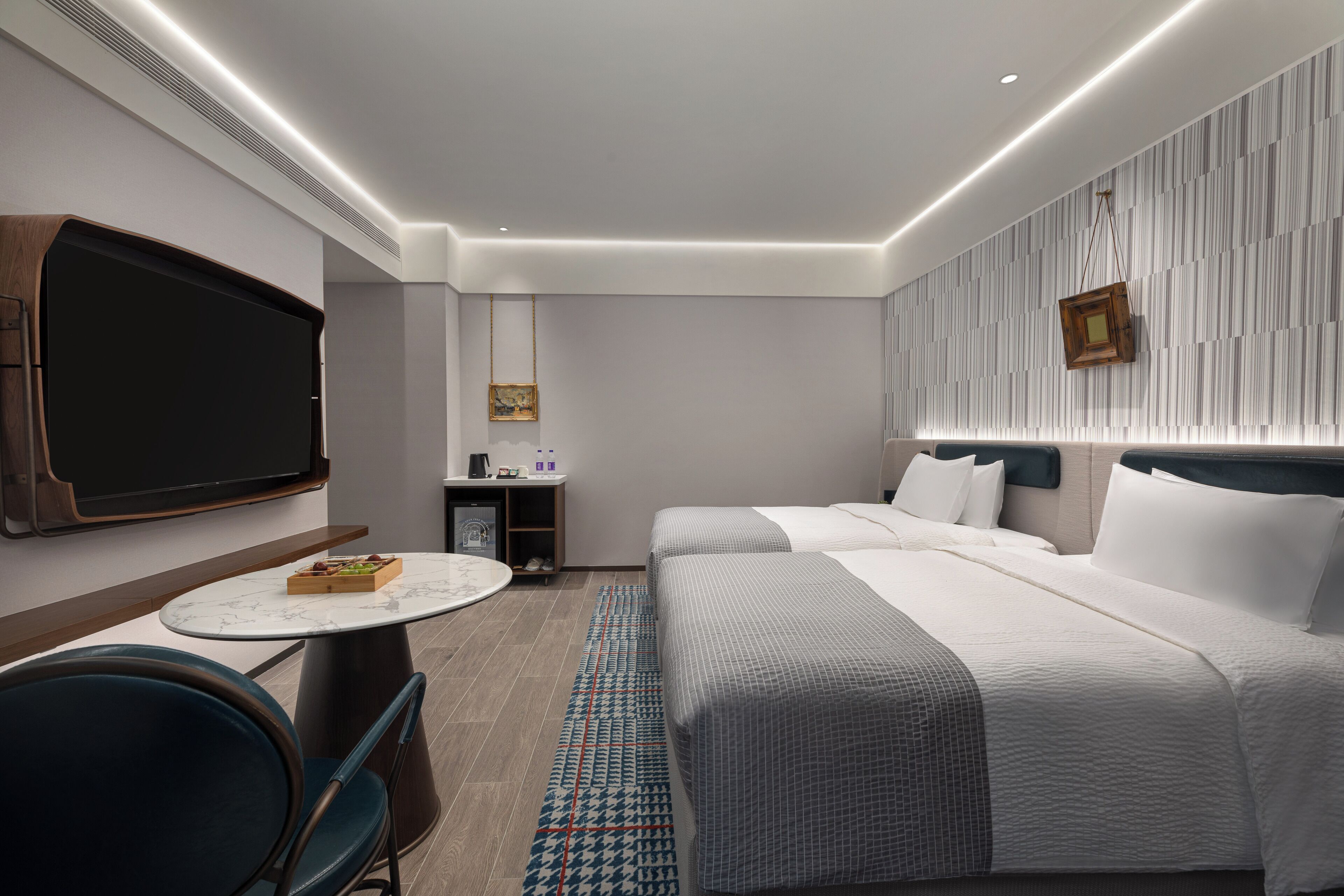 A modern hotel room with a large bed, a desk with a chair, a flat-screen TV, and a small table with a tray of snacks.