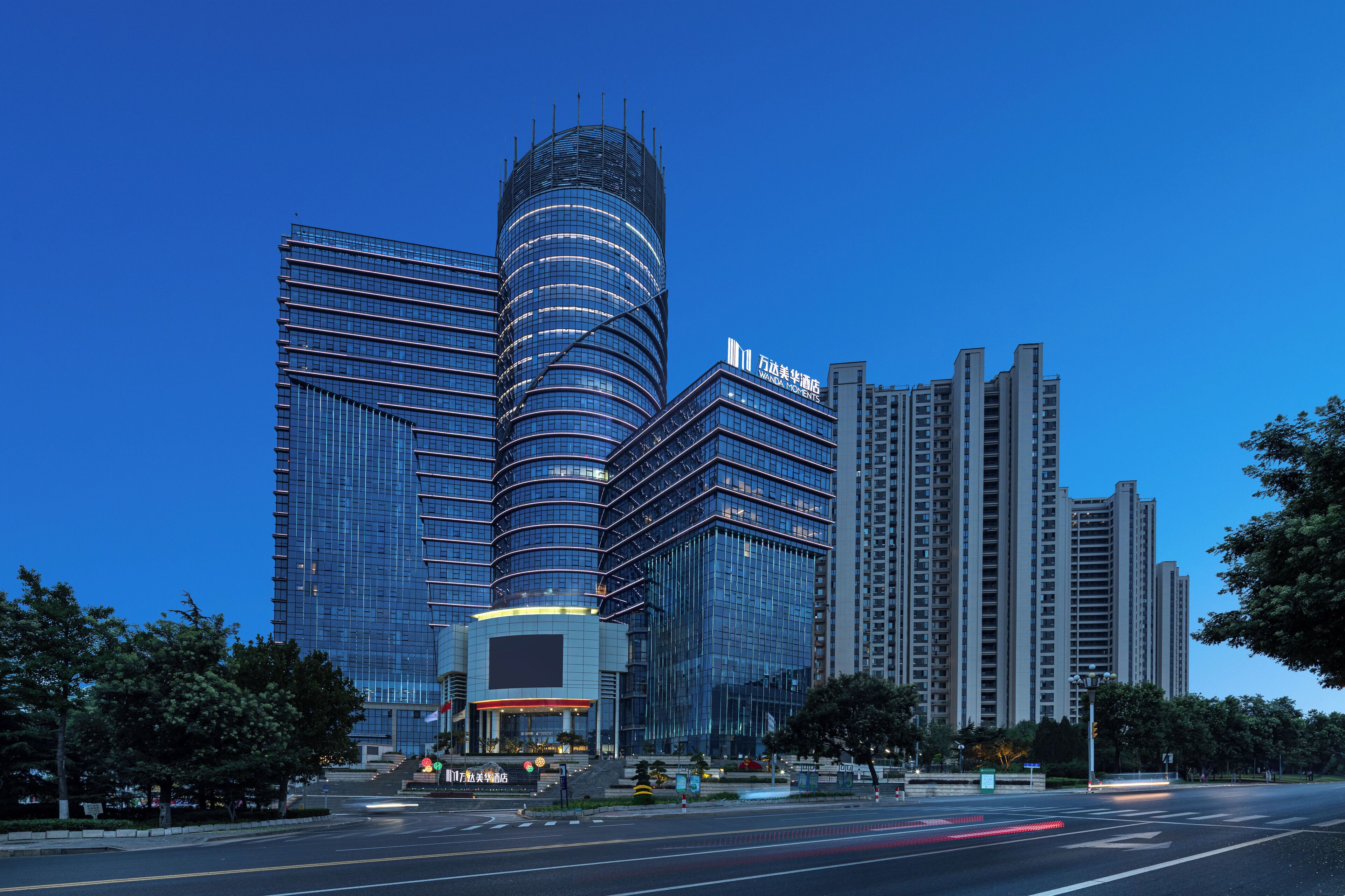 A modern high-rise building with a curved glass facade, multiple floors, and a prominent entrance with a red canopy.