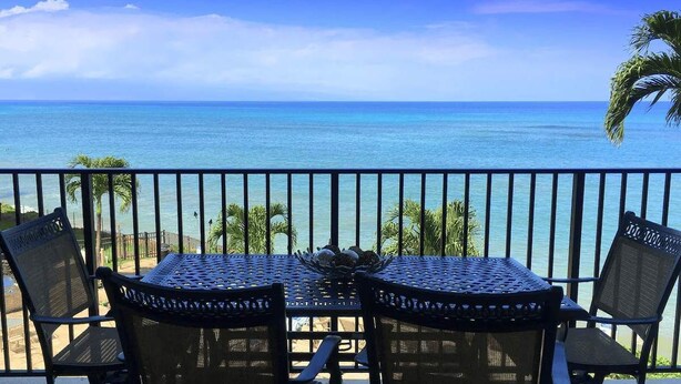 A balcony with a table and chairs overlooking a beach.