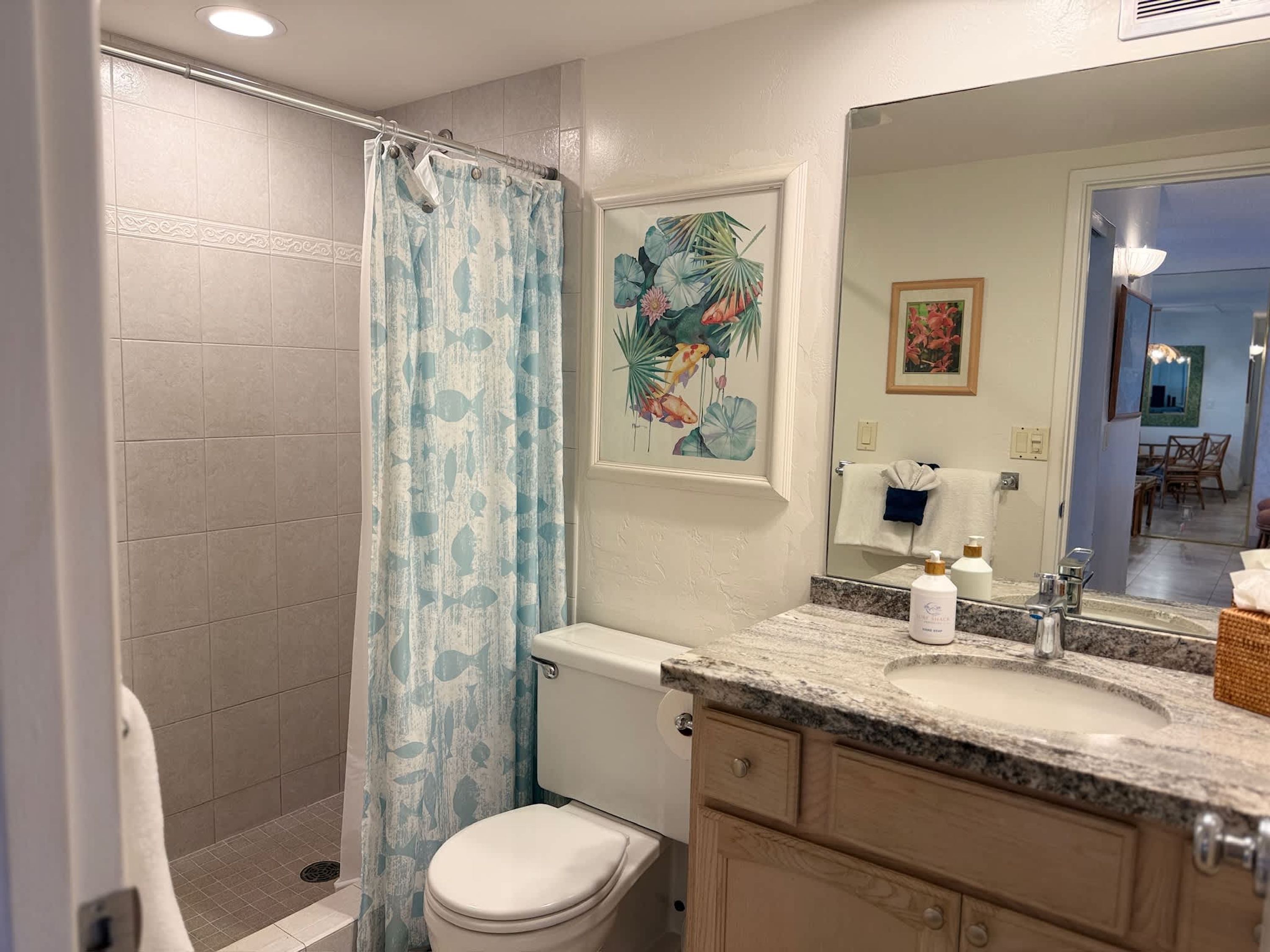 A bathroom with a shower, toilet, sink, and a mirror.