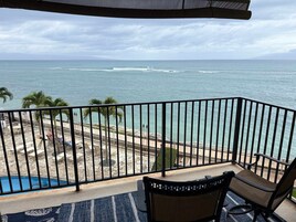 Un balcón con vistas al océano, una piscina y una zona de playa con palmeras.