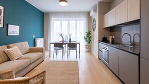 Eine moderne Küche mit Einbauofen und Spüle, ein Essbereich mit Tisch und Stühlen sowie ein Wohnzimmer mit Sofa und Teppich.