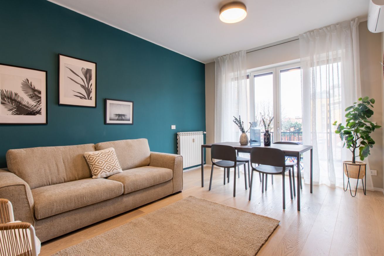 Een woonkamer met een bank, een eettafel met stoelen, lijstwerken aan de muur en een plant in pot.