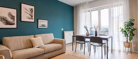 Een woonkamer met een bank, een eettafel met stoelen, lijstwerken aan de muur en een plant in pot.